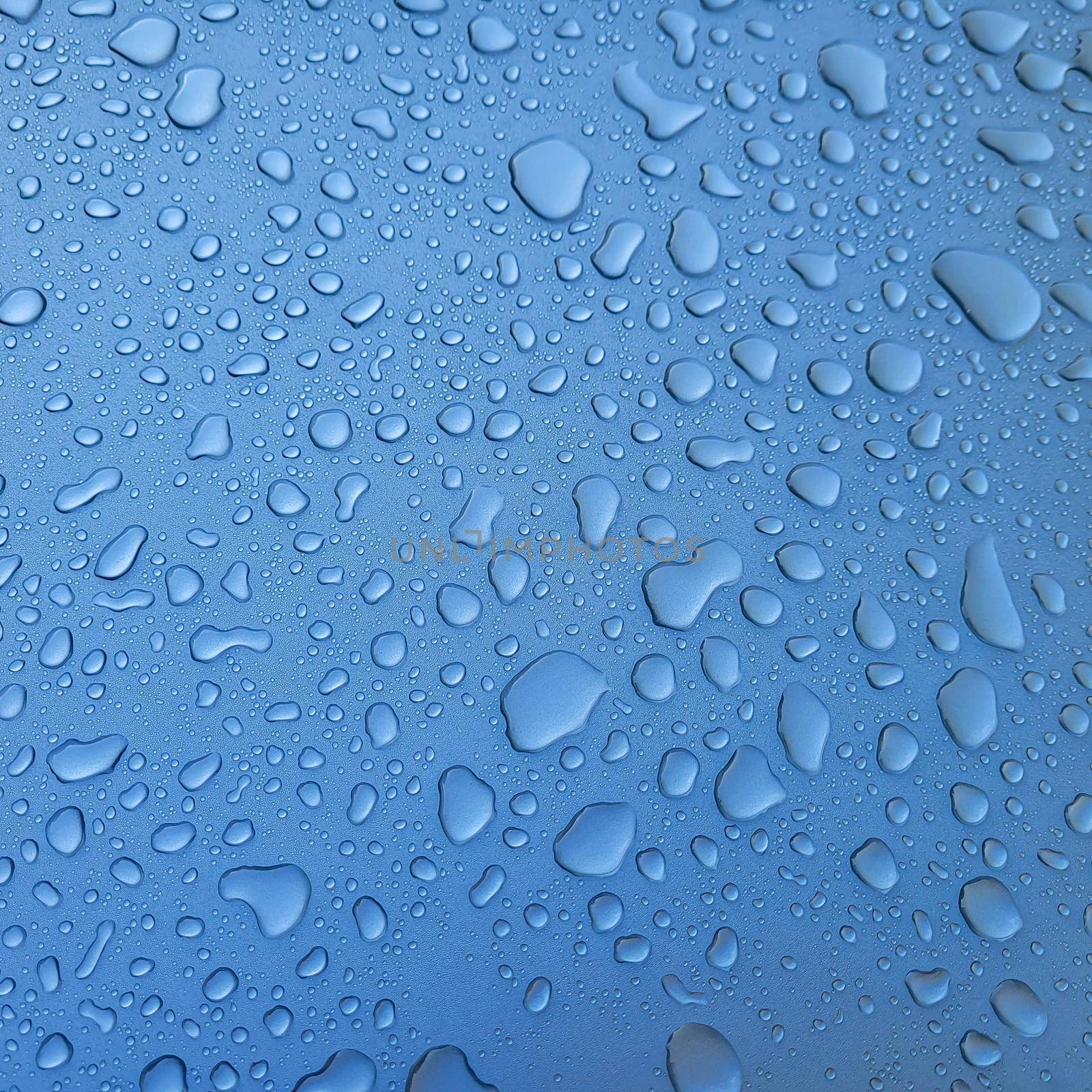 A drop of water on the hood of the car. Water beads after rain or car wash on blue paint surface