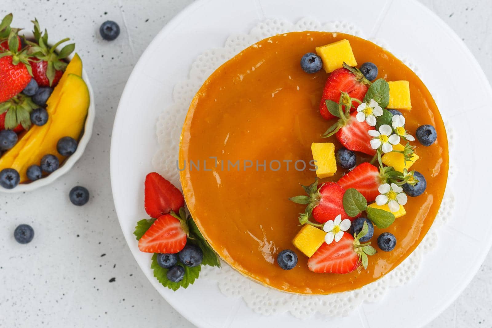 Mango cheesecake decorated with berries, mango slices and flowers on a stand. Top view
