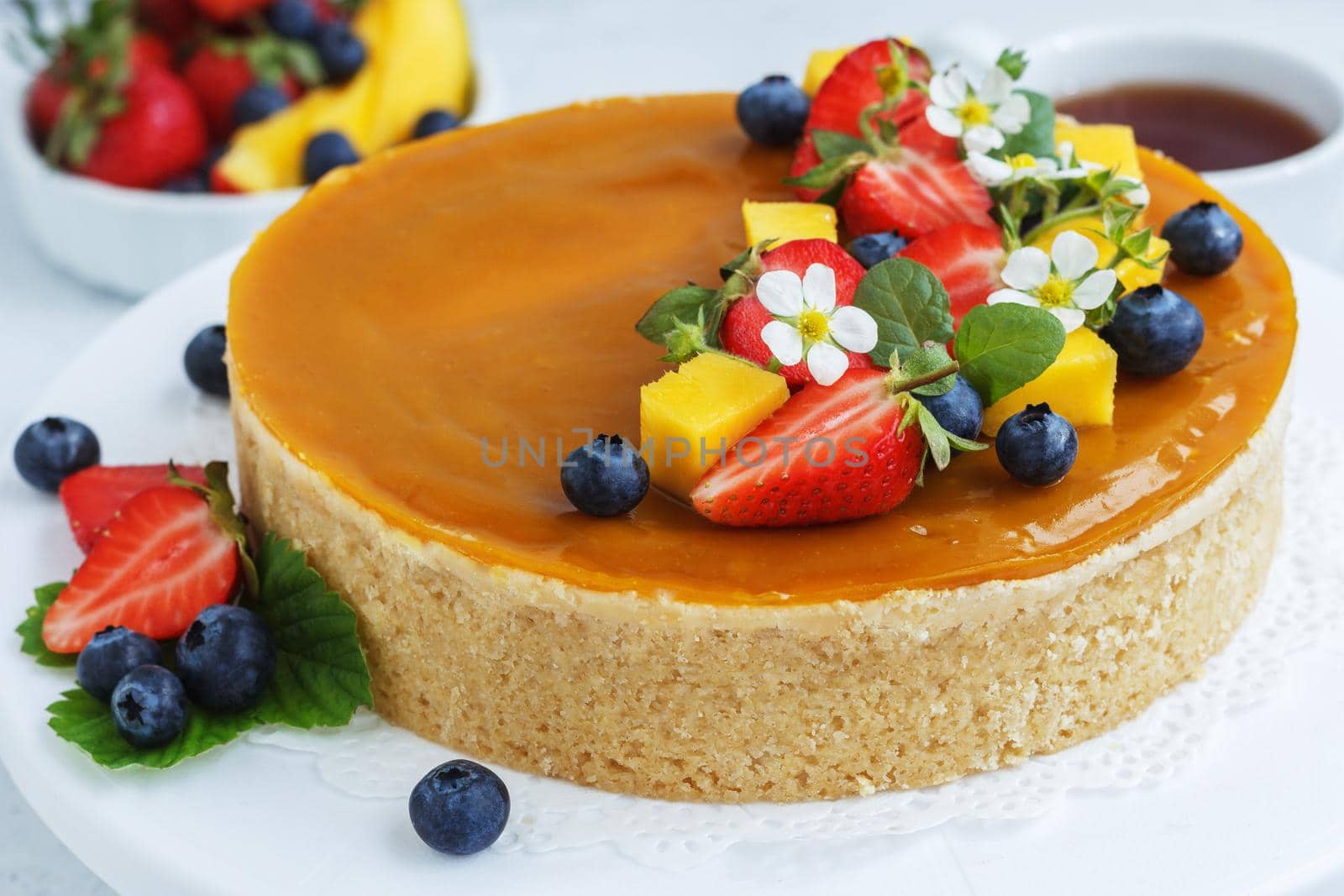 Mango cheesecake decorated with berries, mango slices and flowers on a stand. close-up