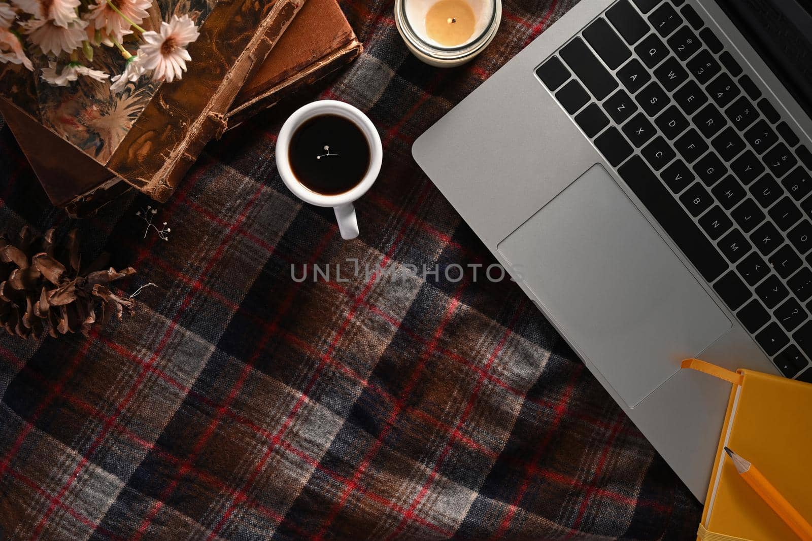 Above view laptop computer, coffee cup, candle and vintage books on plaid background.