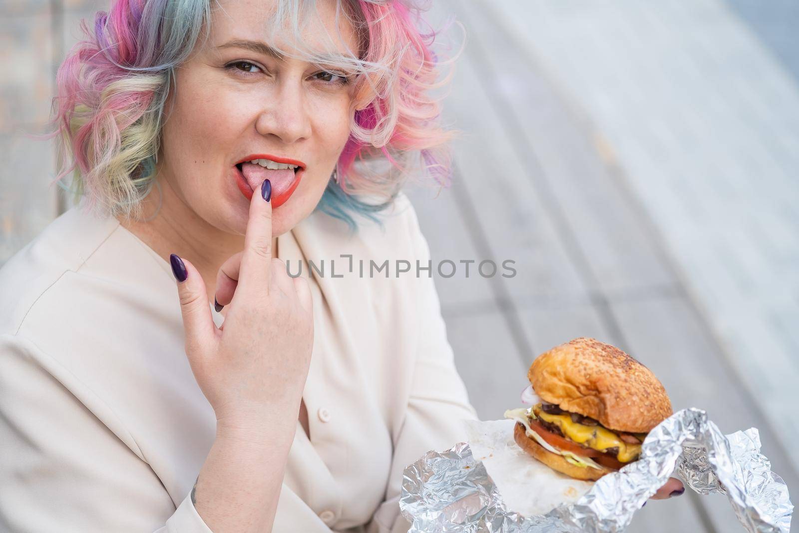 Caucasian woman with curly colored hair eating burger. Bad eating habits and love of fast food by mrwed54