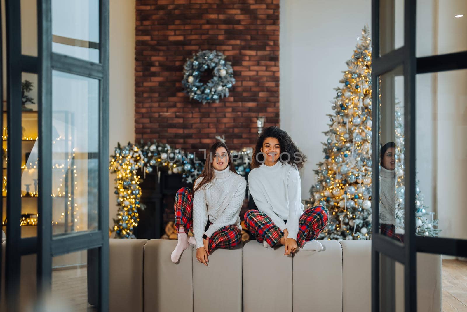 Two female student friends sitting on the couch at home. Multiethnic women.