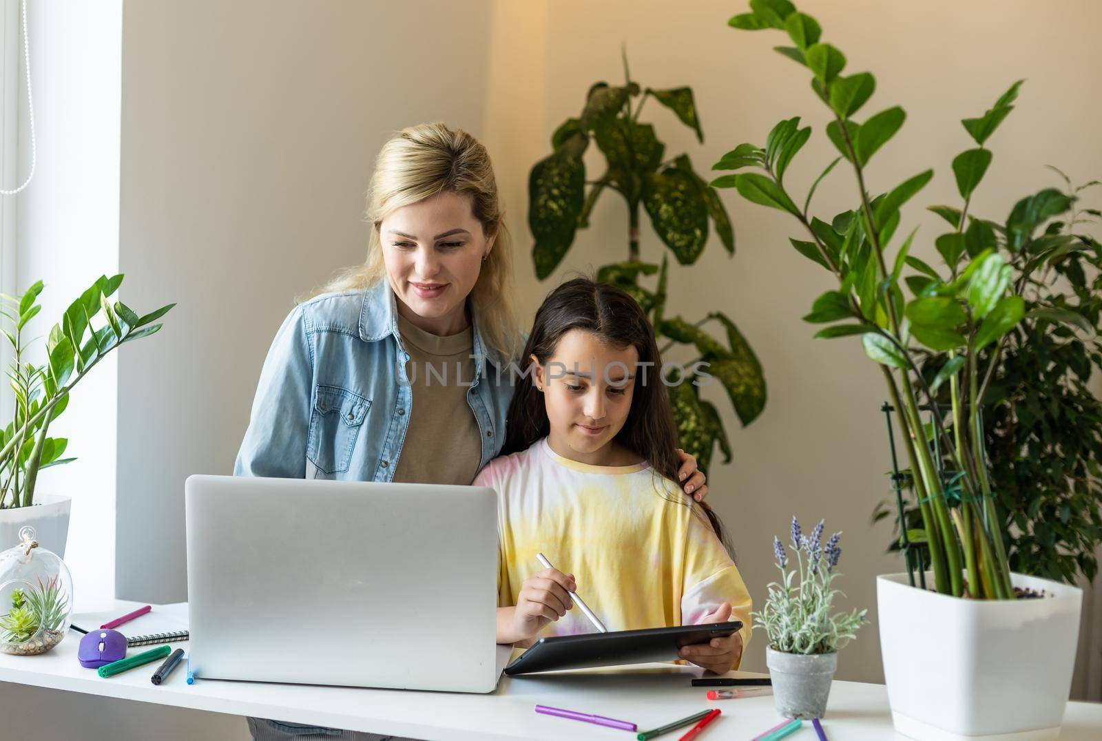 Charming little girl and her beautiful young mom are using a digital tablet and smiling at home.