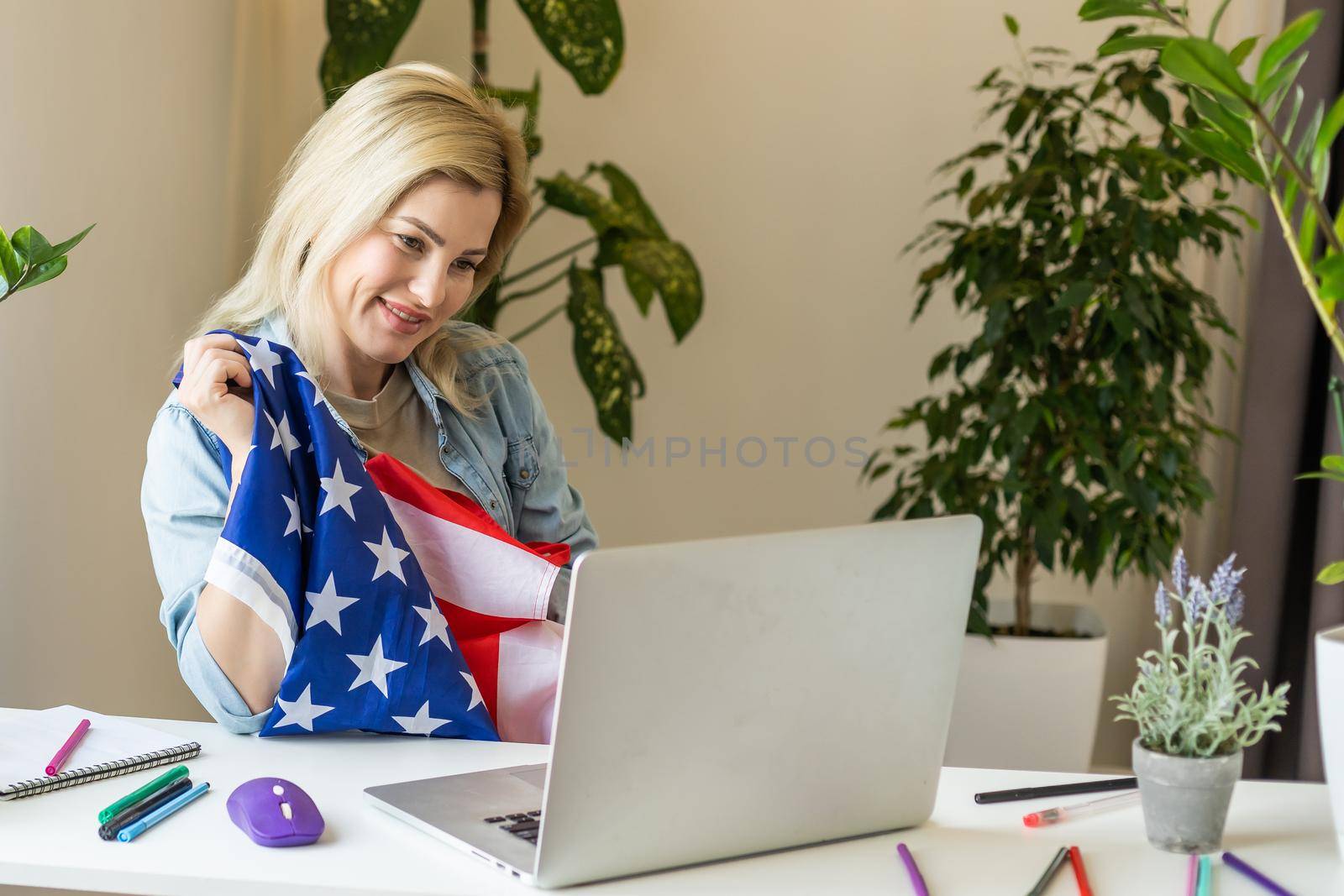 Happy woman employee sitting wrapped in USA flag, shouting for joy in office workplace, celebrating labor day or US Independence day. Indoor studio studio shot isolated on yellow background by Andelov13