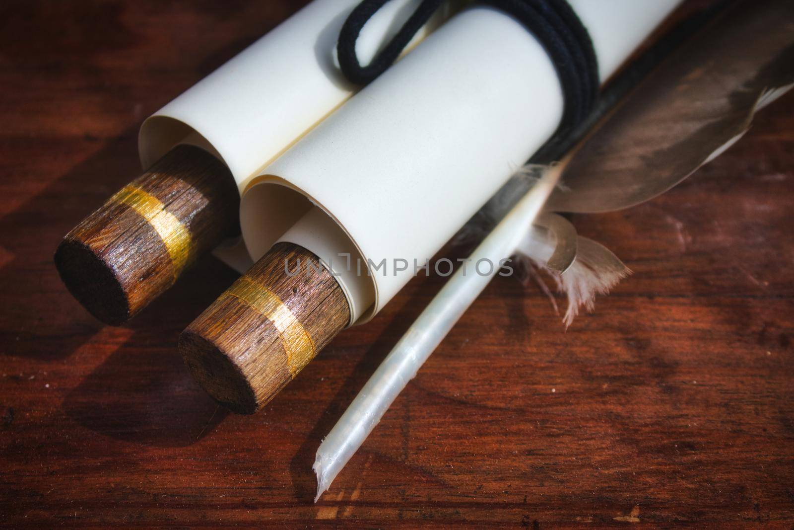 Close-up of old-fashioned paper scroll with a feather quill pen on a wooden table