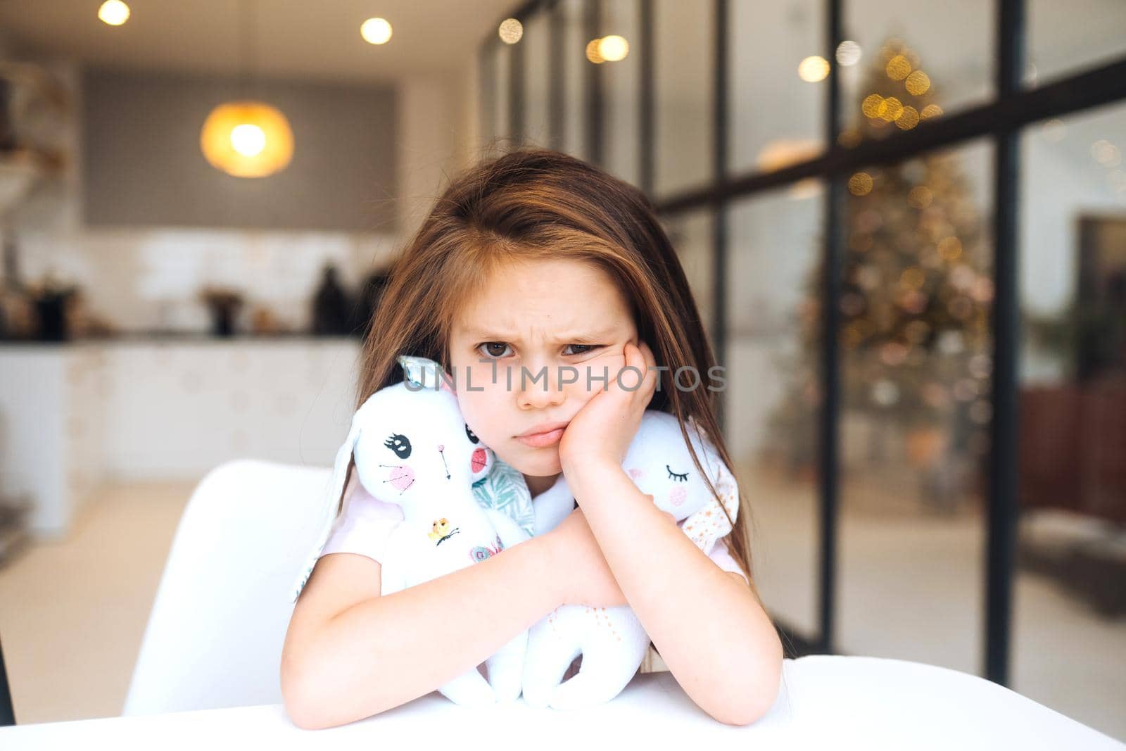 Little sad girl hugging favorite toy while sitting at table happy childhood
