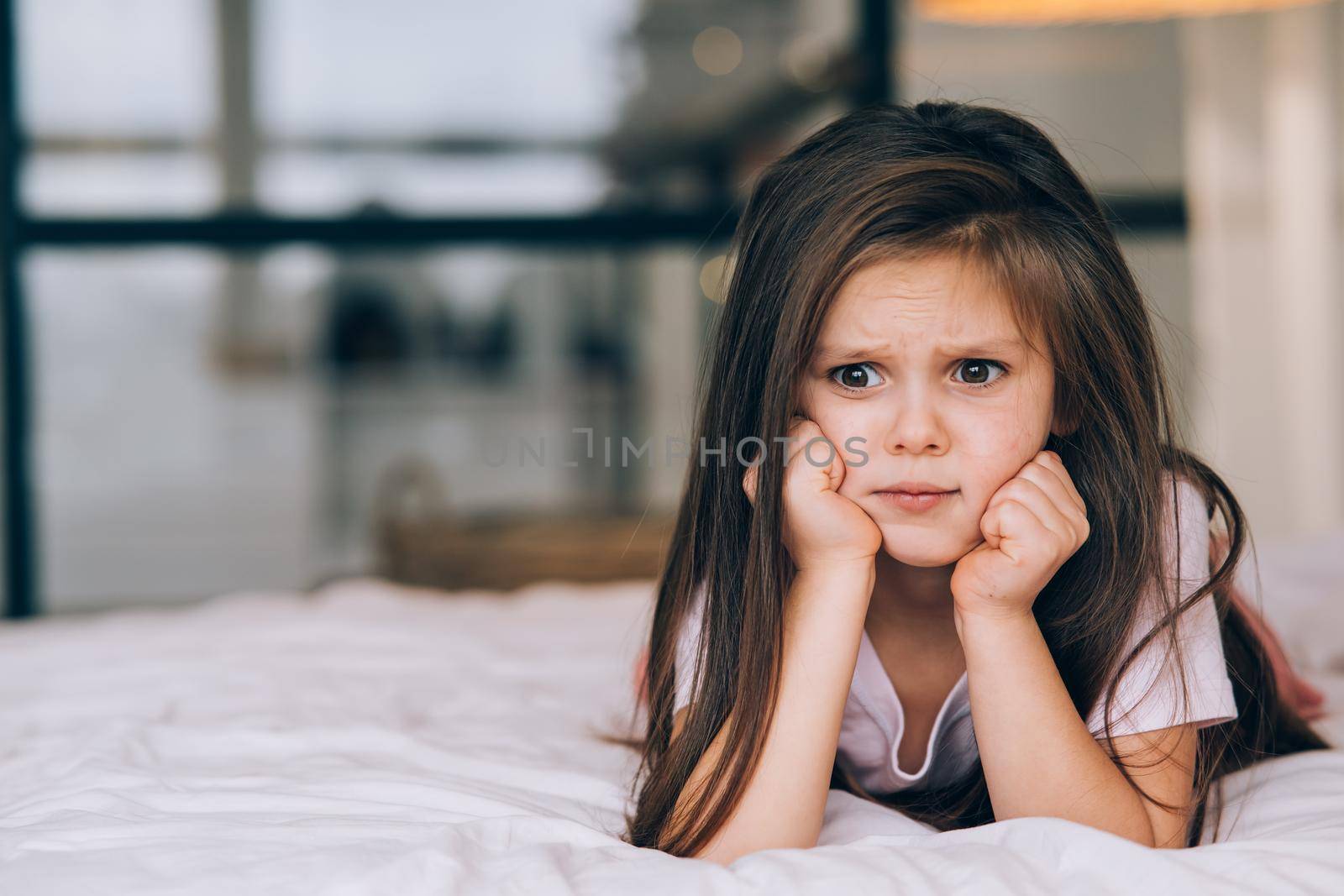 Cute little girl with a sad face lying on the bed. Children emotional concept.