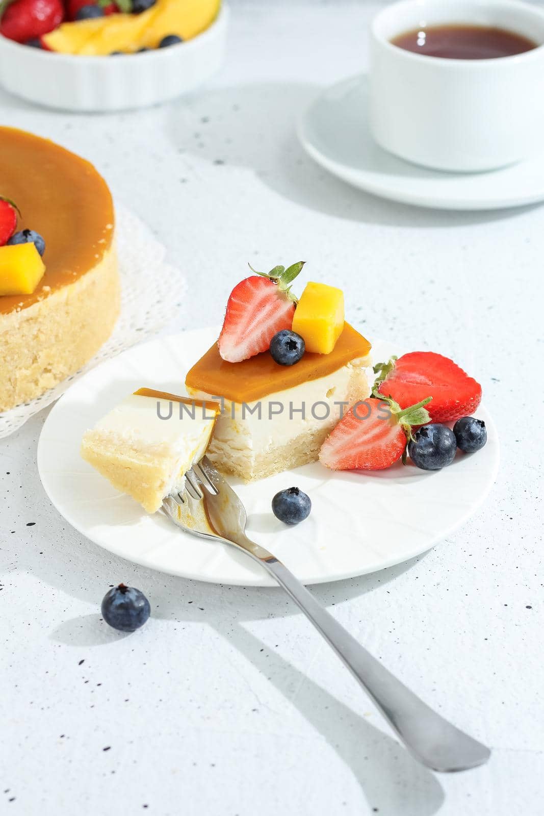 A piece of cheesecake with mango on a plate with a tea fork decorated with berries and flowers on a gray background. Healthy food. by lara29