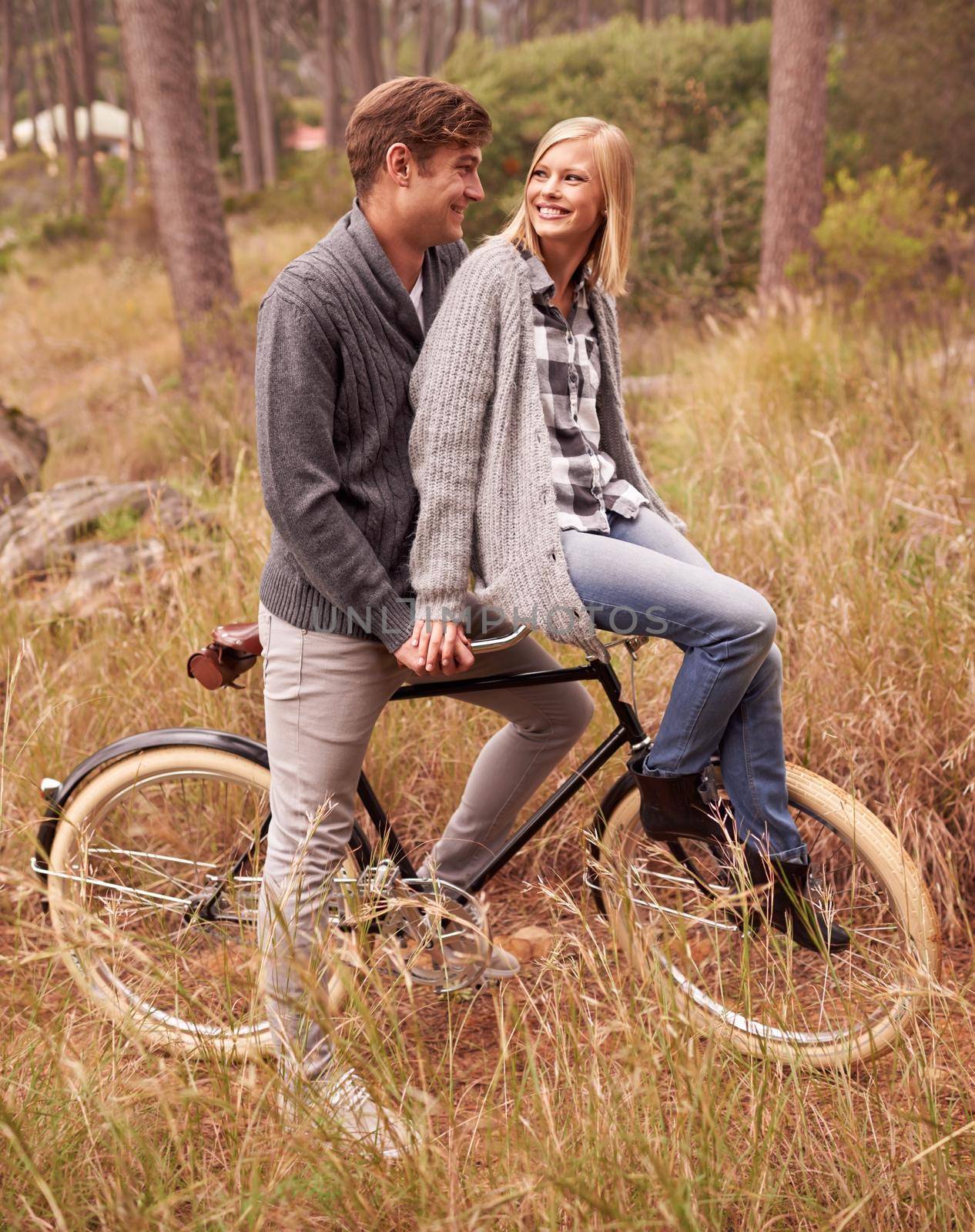 Need a lift. A young couple enjoying a bike ride outdoors together. by YuriArcurs