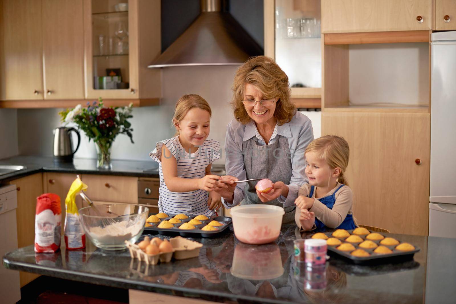 Two little girls baking cupcakes with the help of their grandmother at home.