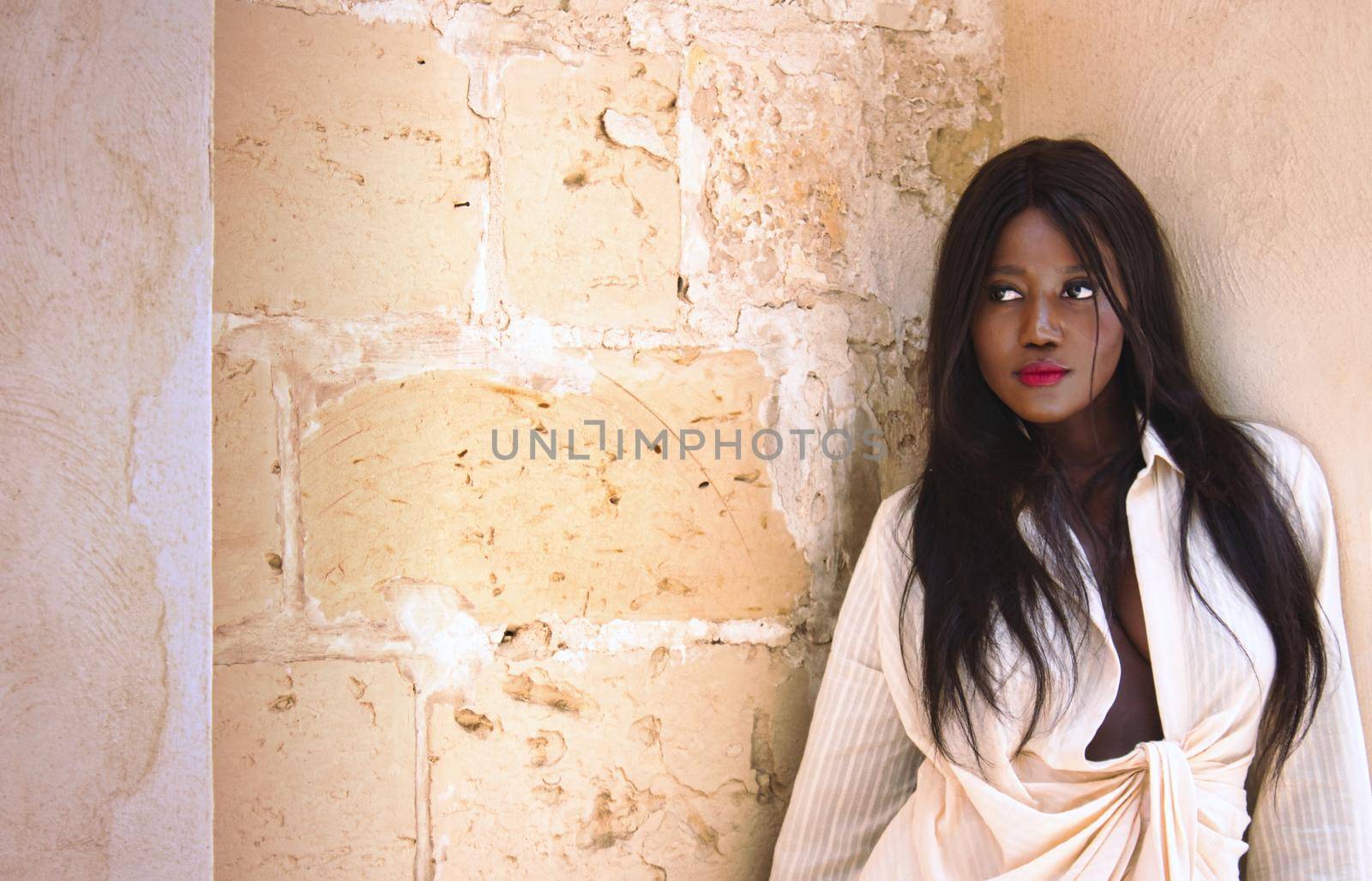 Beautiful young African woman looking to the side standing against a wall by tennesseewitney