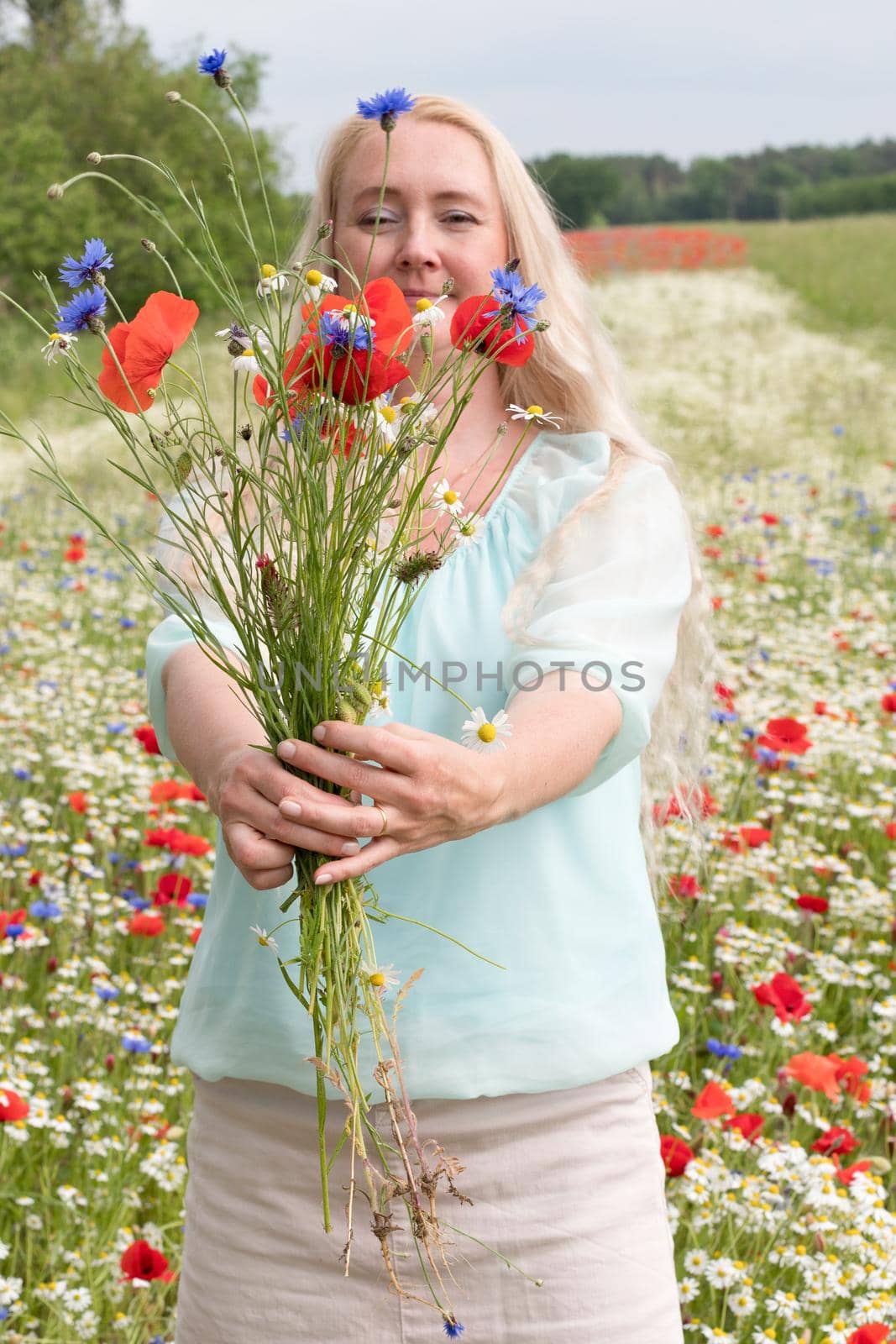 beautiful middle-aged blonde woman stands among a flowering field of poppies by KaterinaDalemans