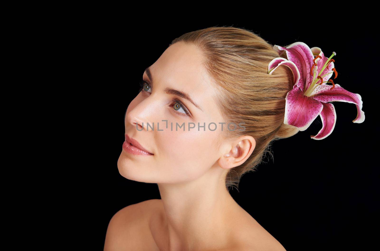 An attractive young woman with a flower in her hair against a black background.