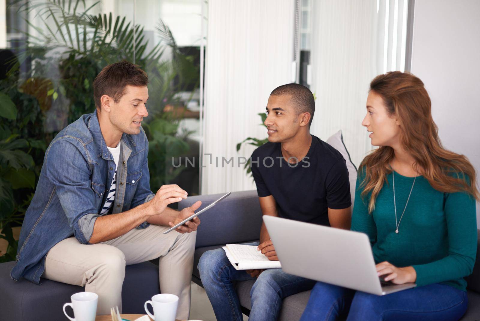 A team of young business professionals using technology in an informal meeting.