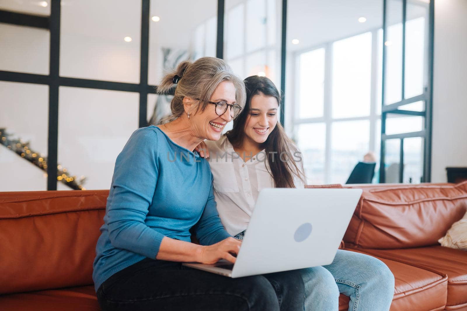 Mother and daughter sitting on couch and watching something on laptop at home