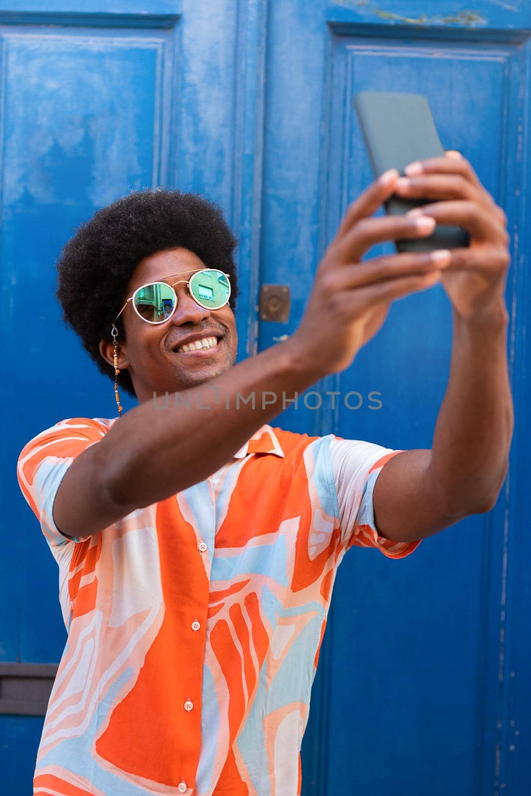 Young happy black man taking selfie with mobile phone outdoors. Vertical image. by Hoverstock