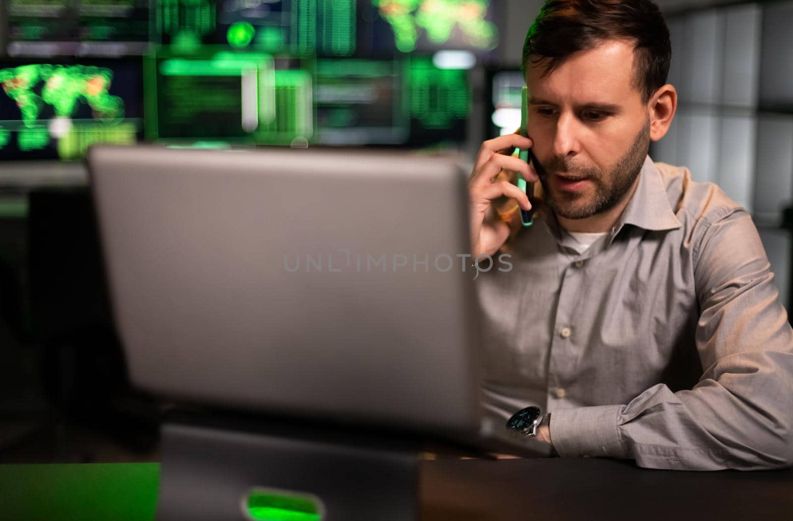 Male stock market trader working in office using laptop and talking on mobile phone with client. Financial adviser concept.