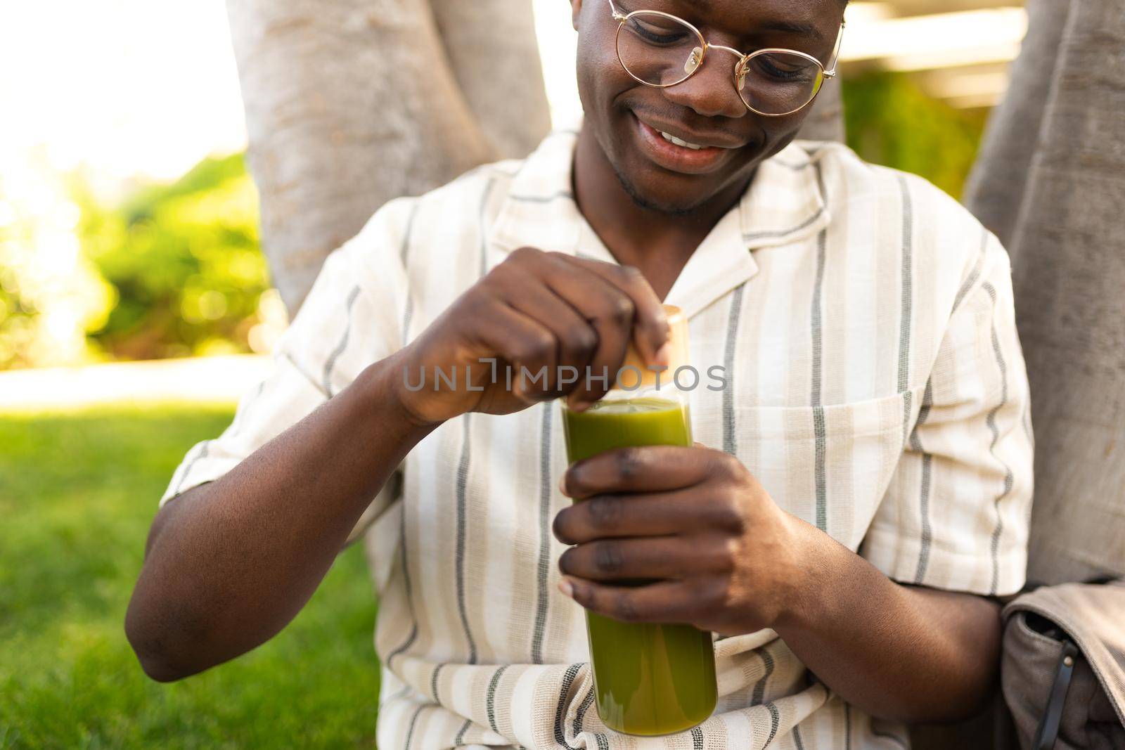 Young black man opening glass bottle of green juice outdoors. by Hoverstock