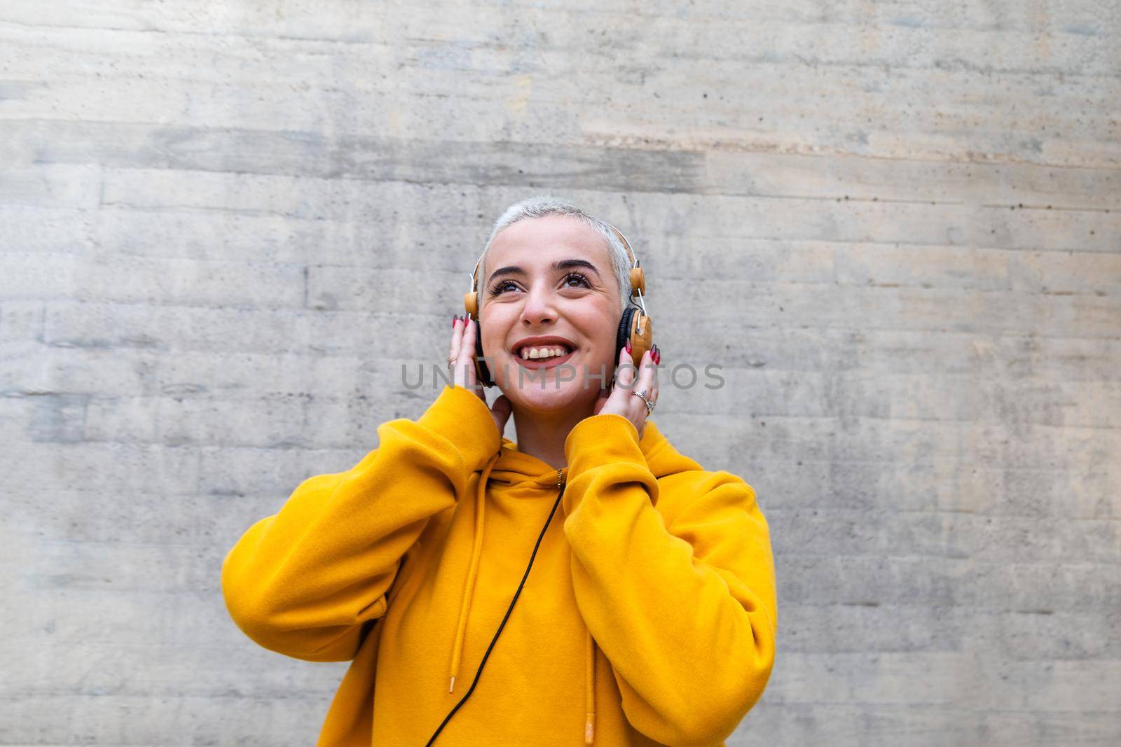 Gen z female teenager with platinum blonde buzz cut listening to music with wireless headphones.Lifestyle concept.
