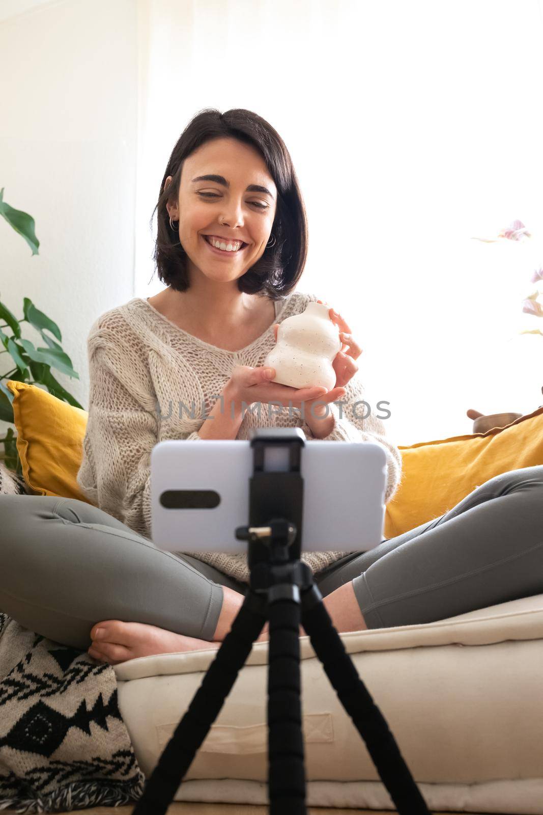 Young caucasian woman DIY influencer showing handmade artisan ceramic vase at camera recording online video. Vertical image. Social media interior design concept.