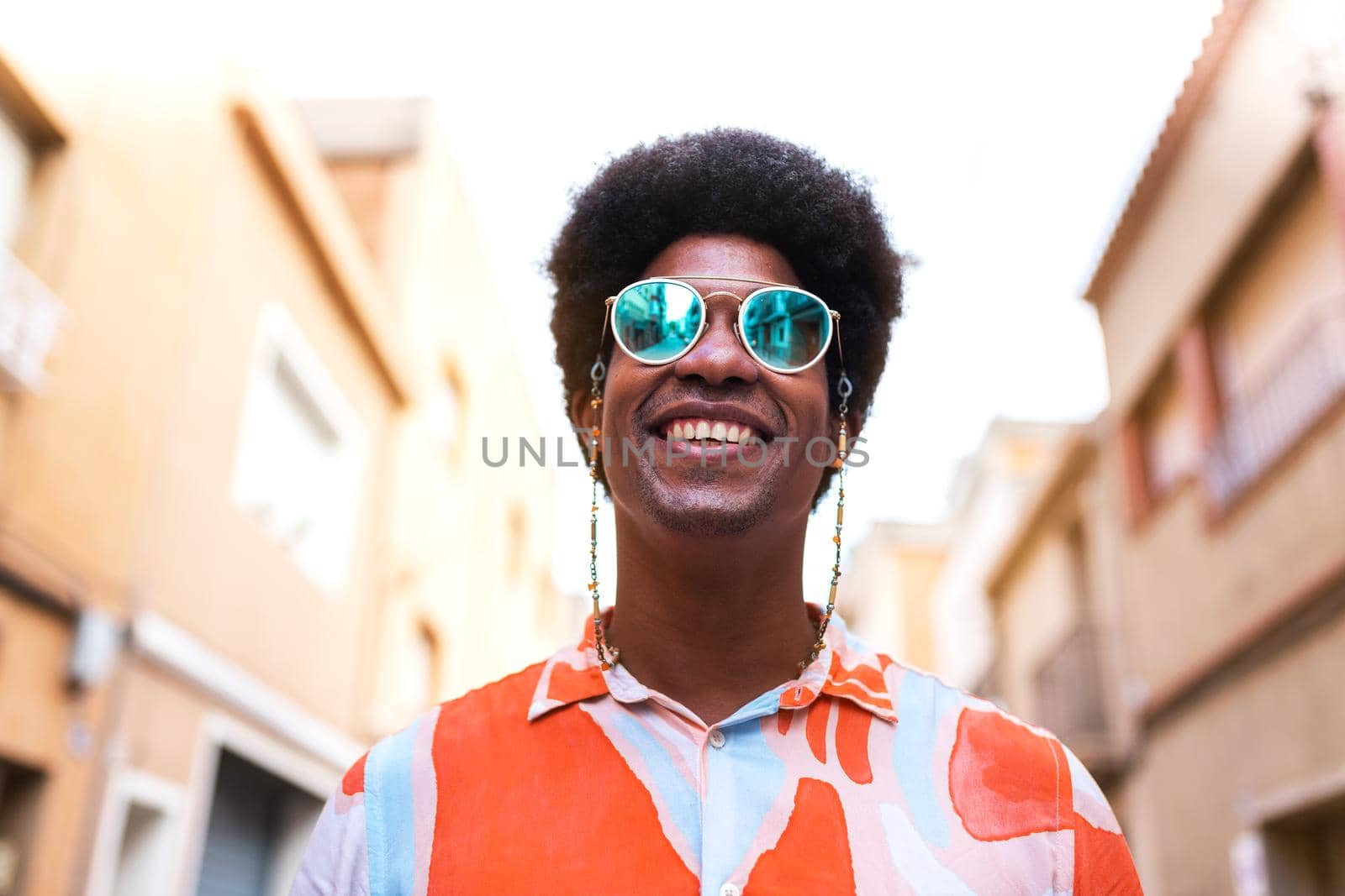 Portrait of young happy and smiling black man wearing sunglasses outdoors. by Hoverstock