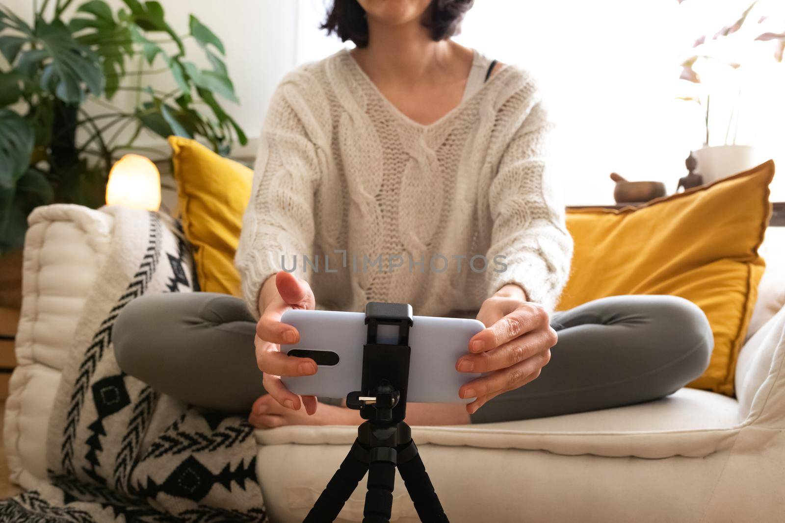 Unrecognizable young caucasian woman setting up smartphone to record herself for online video. Inflluencer live streaming. Social media concept.