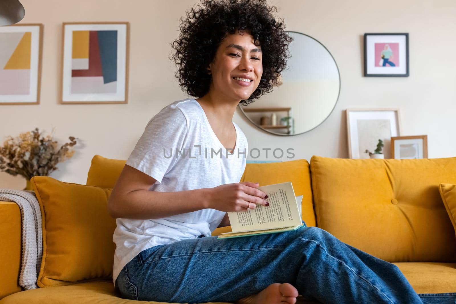Portrait of smiling, happy young African American woman reading a book at home looking at camera. Lifestyle concept.