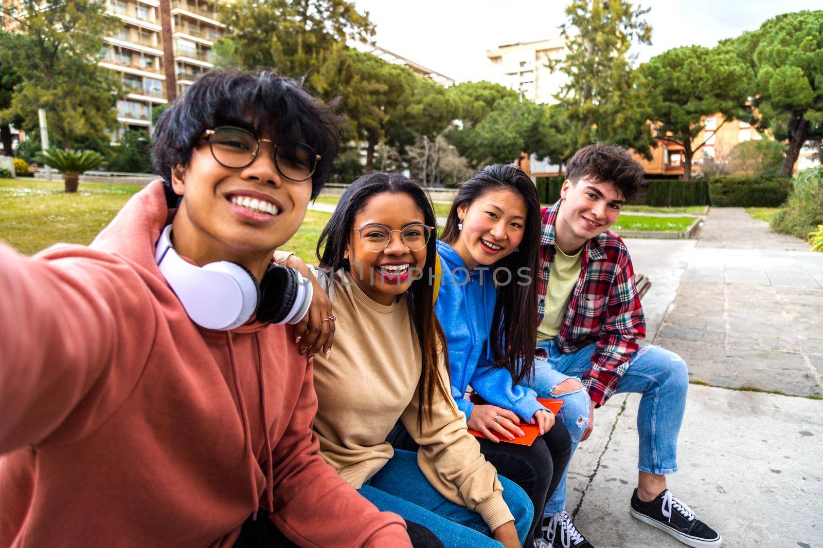Group of multiracial college student friends taking selfie with phone outside. Students laughing and having fun in park. by Hoverstock