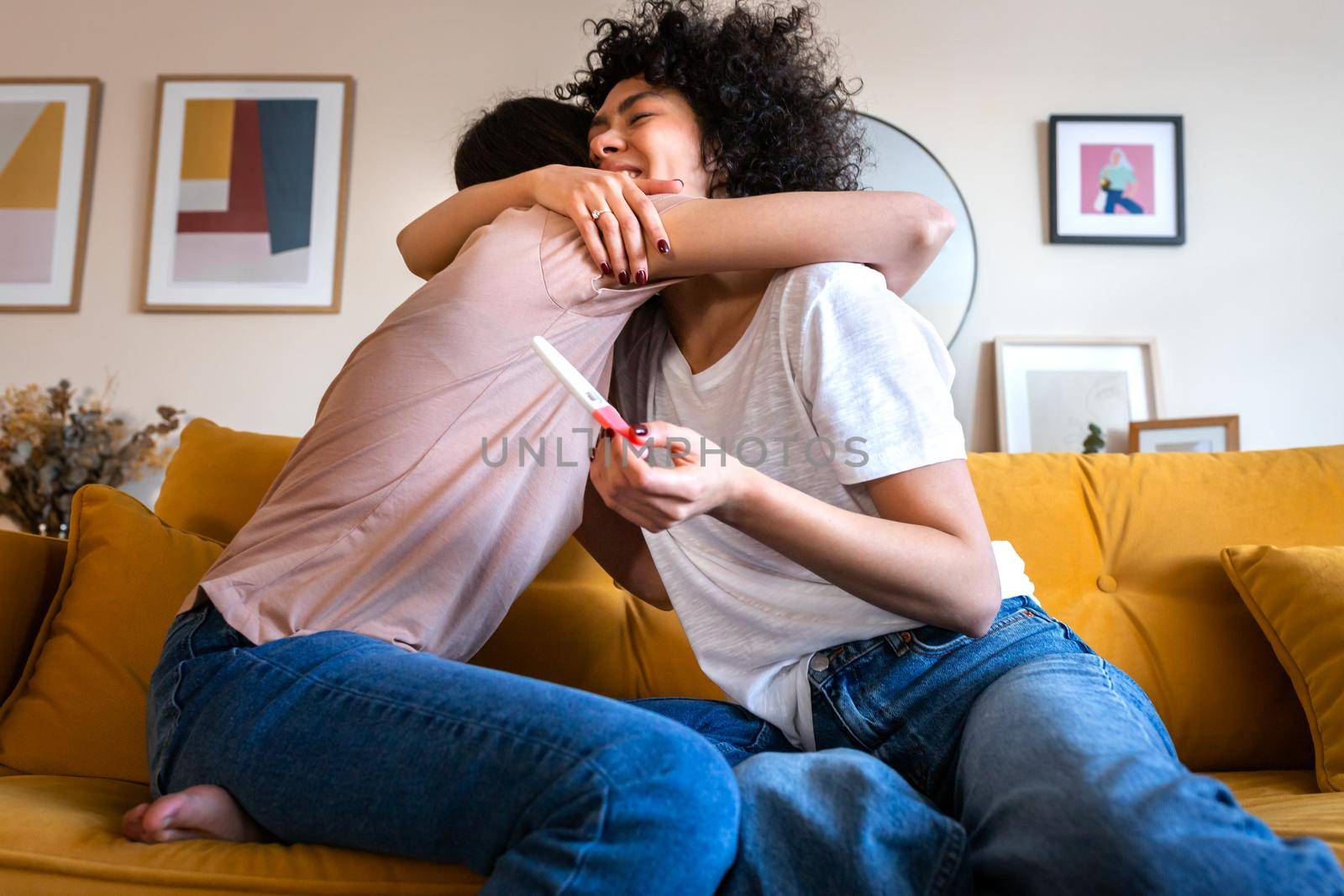 Happy multiracial lesbian couple embrace celebrating positive pregnancy test result. by Hoverstock