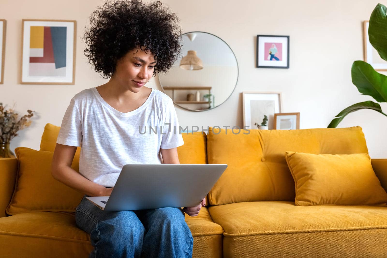 Young African american woman sitting on the couch using laptop working at home. Copy space. by Hoverstock