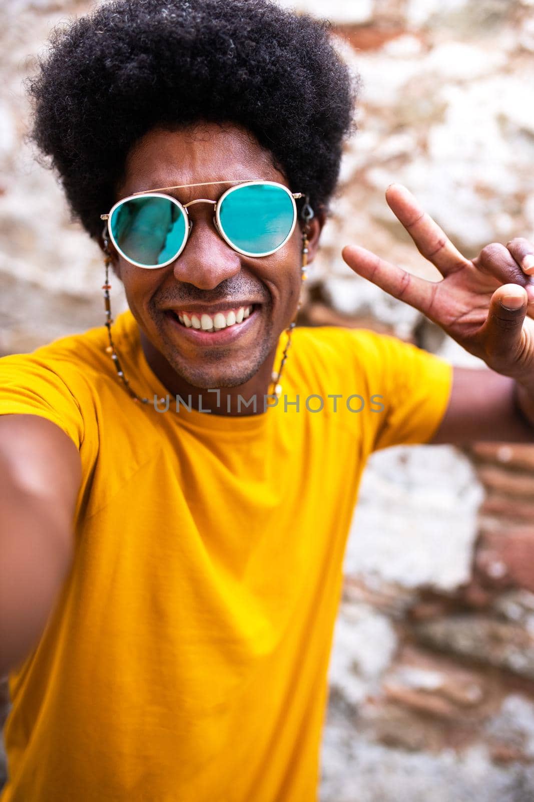 Happy, smiling young African American man taking selfie making peace sign. Copy space. Brick wall background. Vertical image. Lifestyle concept.