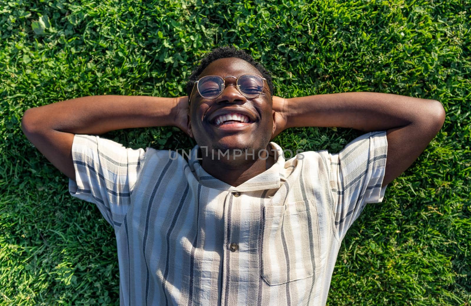 Top view of black man relaxing on grass. Happy black male lying on grass, smiling, enjoying life. Relaxation concept.