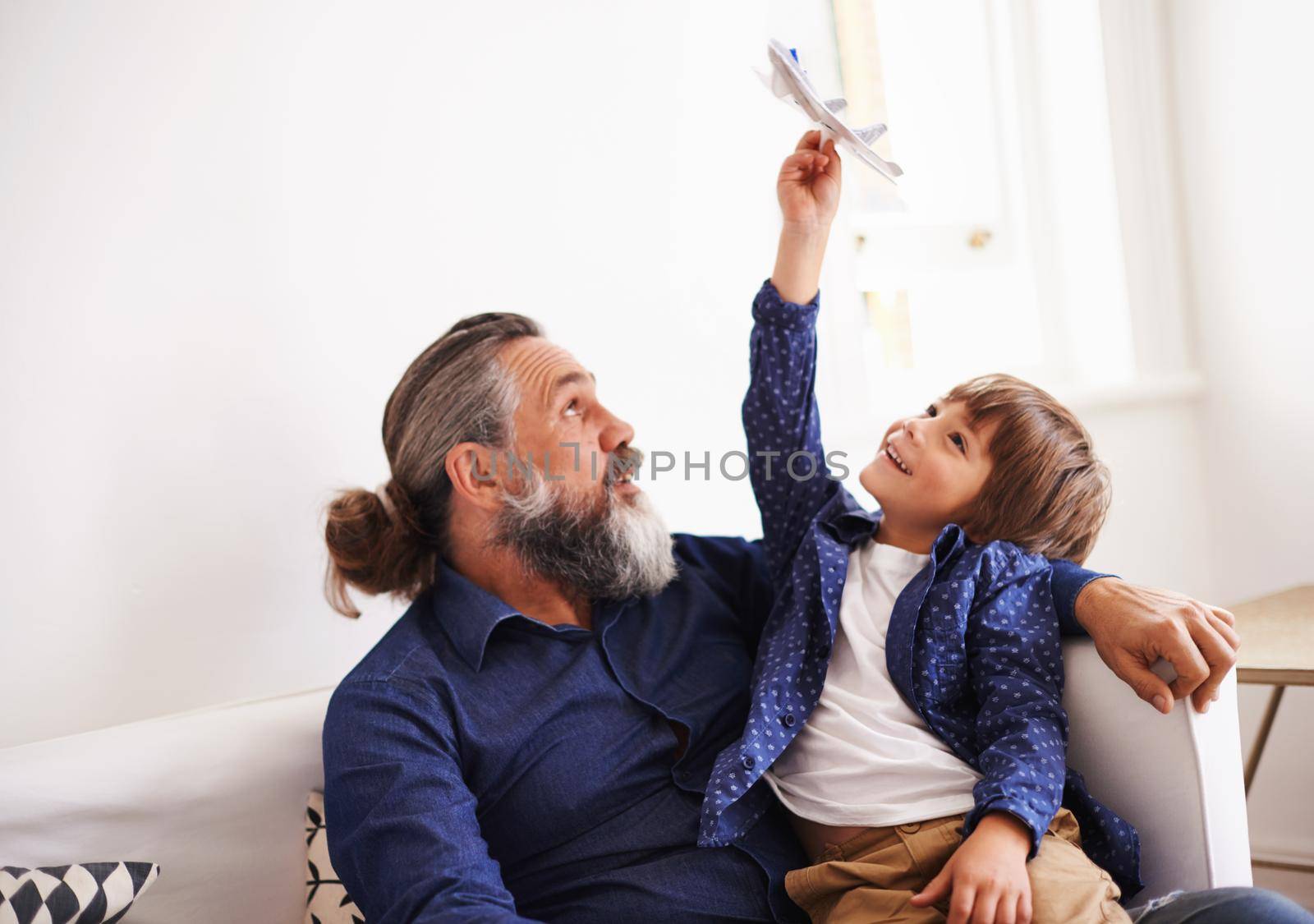 Awesome air maneuvers with grandpa. Cropped shot of a young boy sitting on his grandfathers lap playing with a toy jet. by YuriArcurs