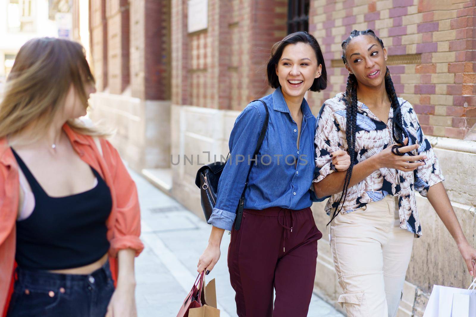 Positive multiethnic women walking together after shopping by javiindy