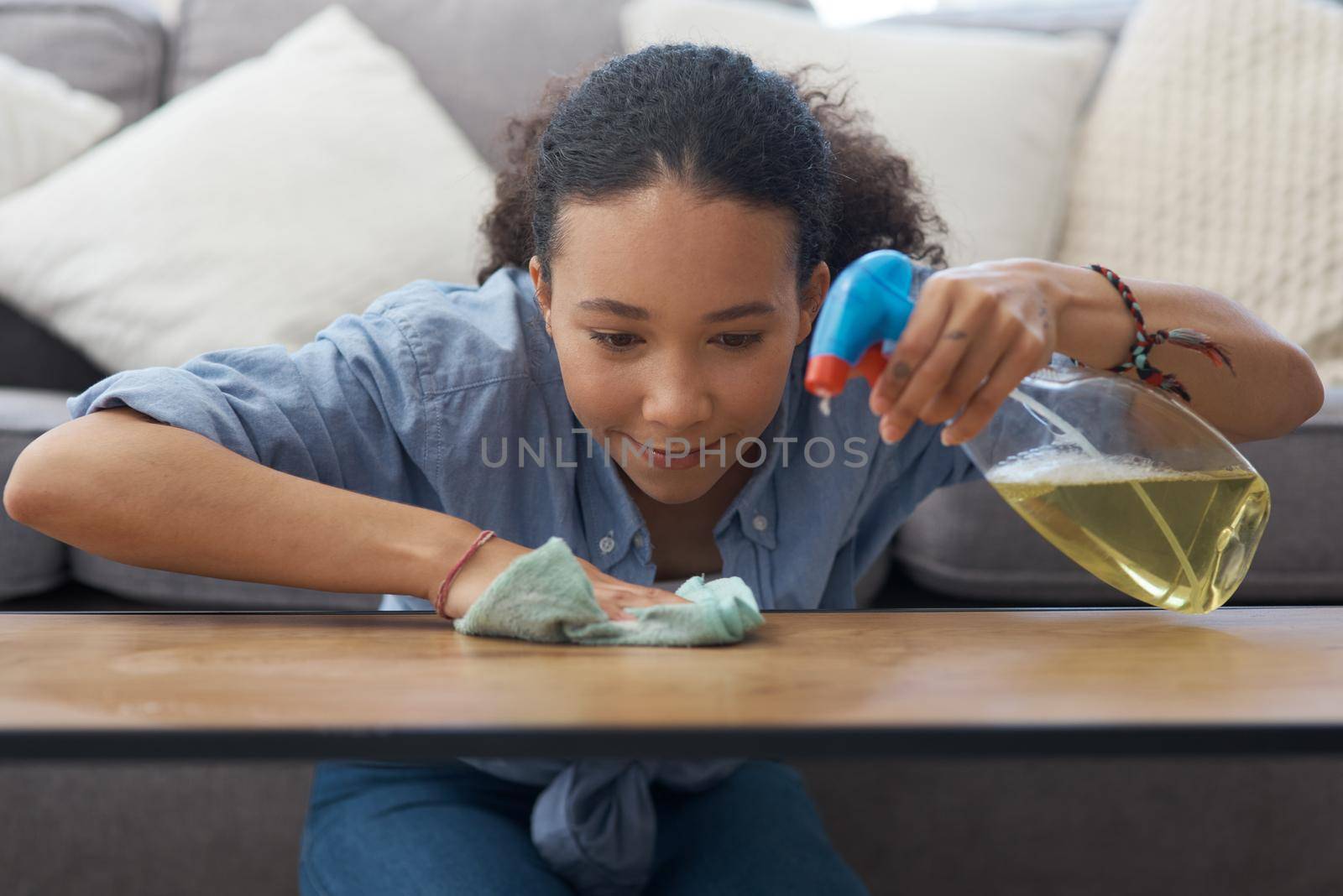 Shot of a young woman wiping down her wooden coffee table in her living room at home.