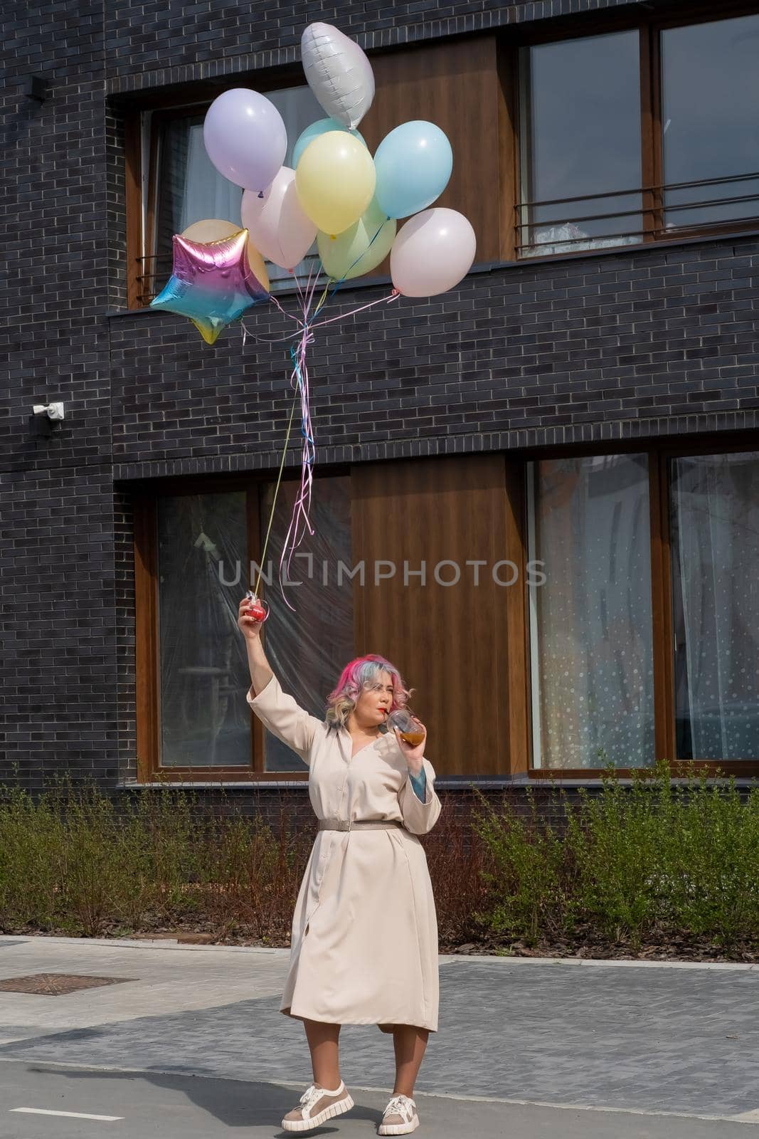 Woman in colored hair walks with an armful of balloons and drinks a refreshing beverage by mrwed54