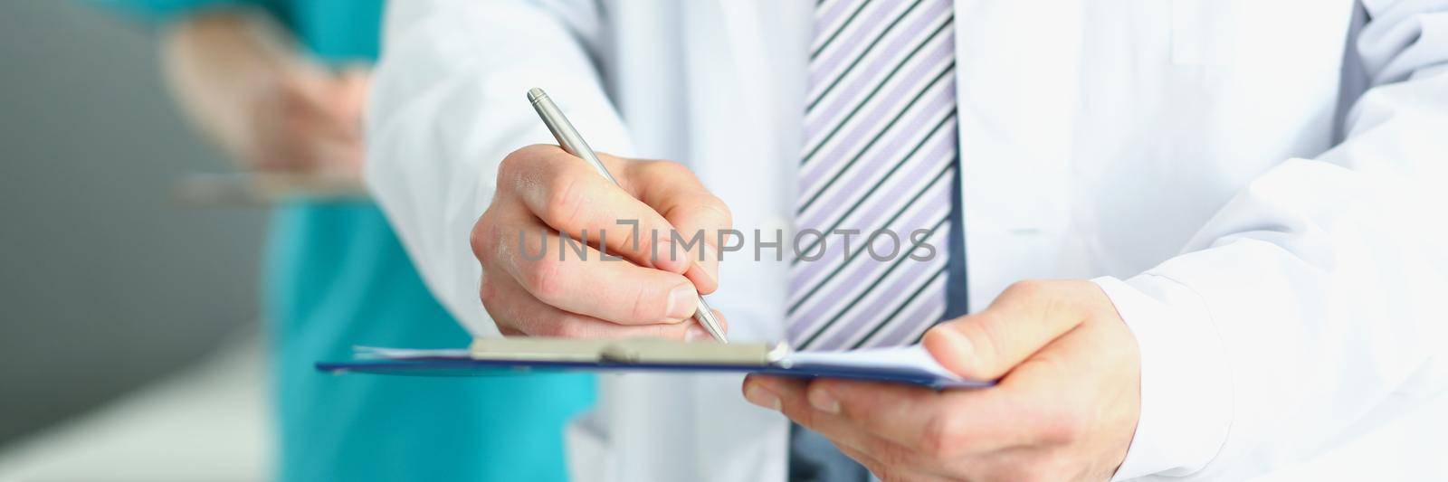 The doctor holds a folder in his hands and writes, close-up, blurred background. Medical professionals make records of diseases, write prescriptions