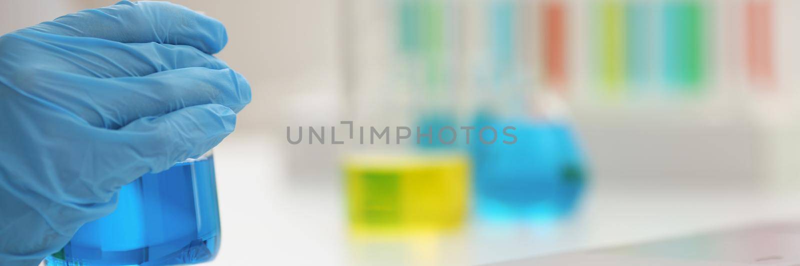 Microbiologist hands in gloves hold blue liquid, close-up, blurry background. Chemical experiments in the laboratory