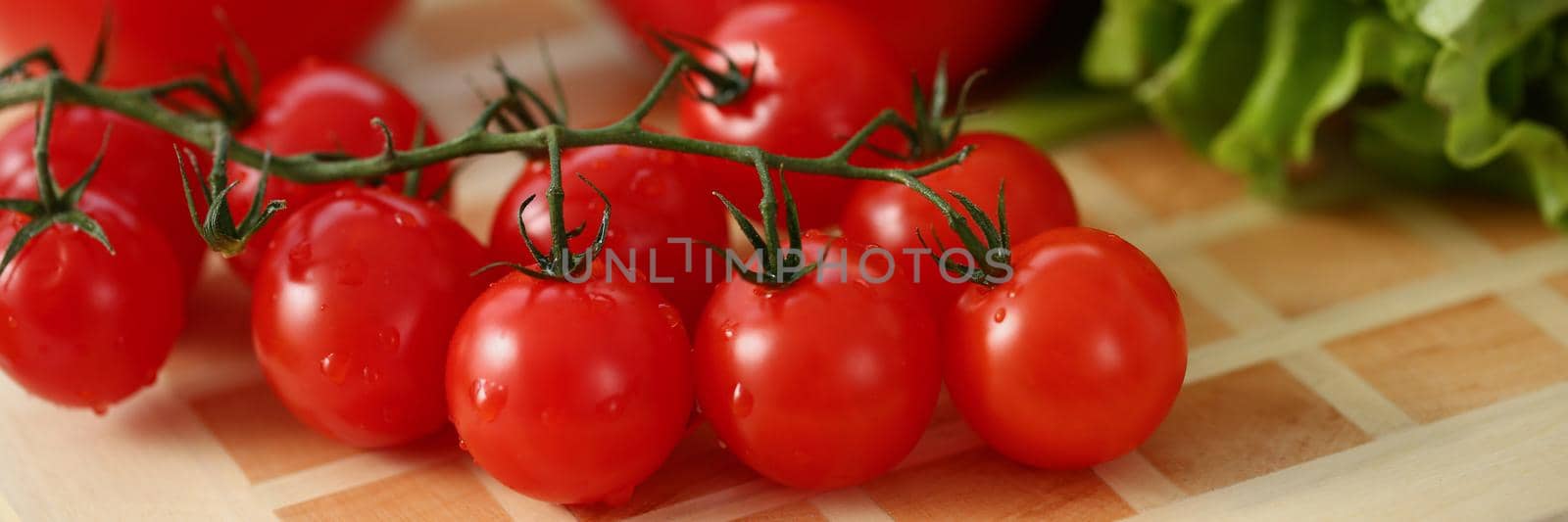 On the table are red tomatoes and green salad, close-up, blurry. Ripe bright beautiful vegetables, organic product