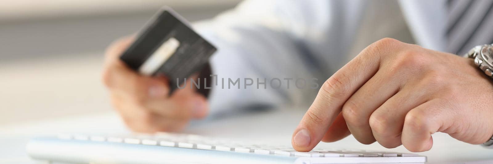 A man with a credit card in his hand is typing on the keyboard, close-up, blurry. Online shopping, banking application