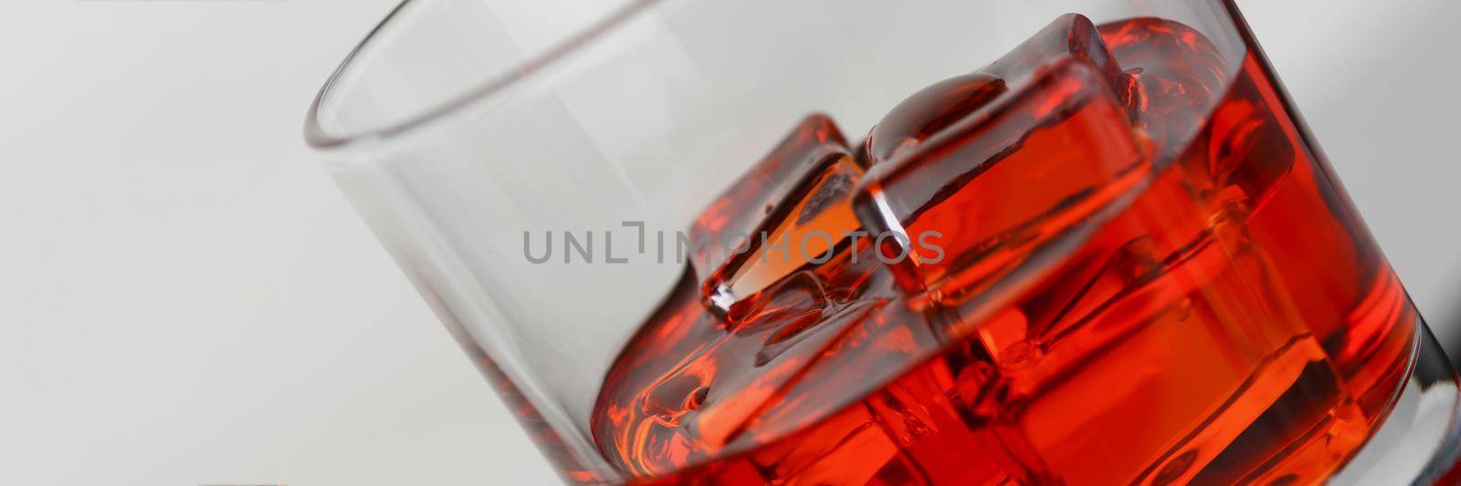 Glass of brown alcoholic drink with ice, close-up. Summer tonic drink on gray background, cocktail, sweet water