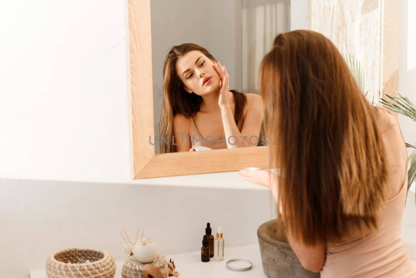 Serious young woman moisturizes face skin with cream in the morning in the bathroom. The concept of clean skin, facial care