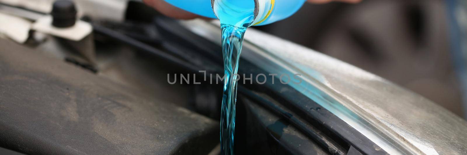 A man pours antifreeze from a canister into a car engine, close-up. Blue coolant, anti-corrosion properties, service station