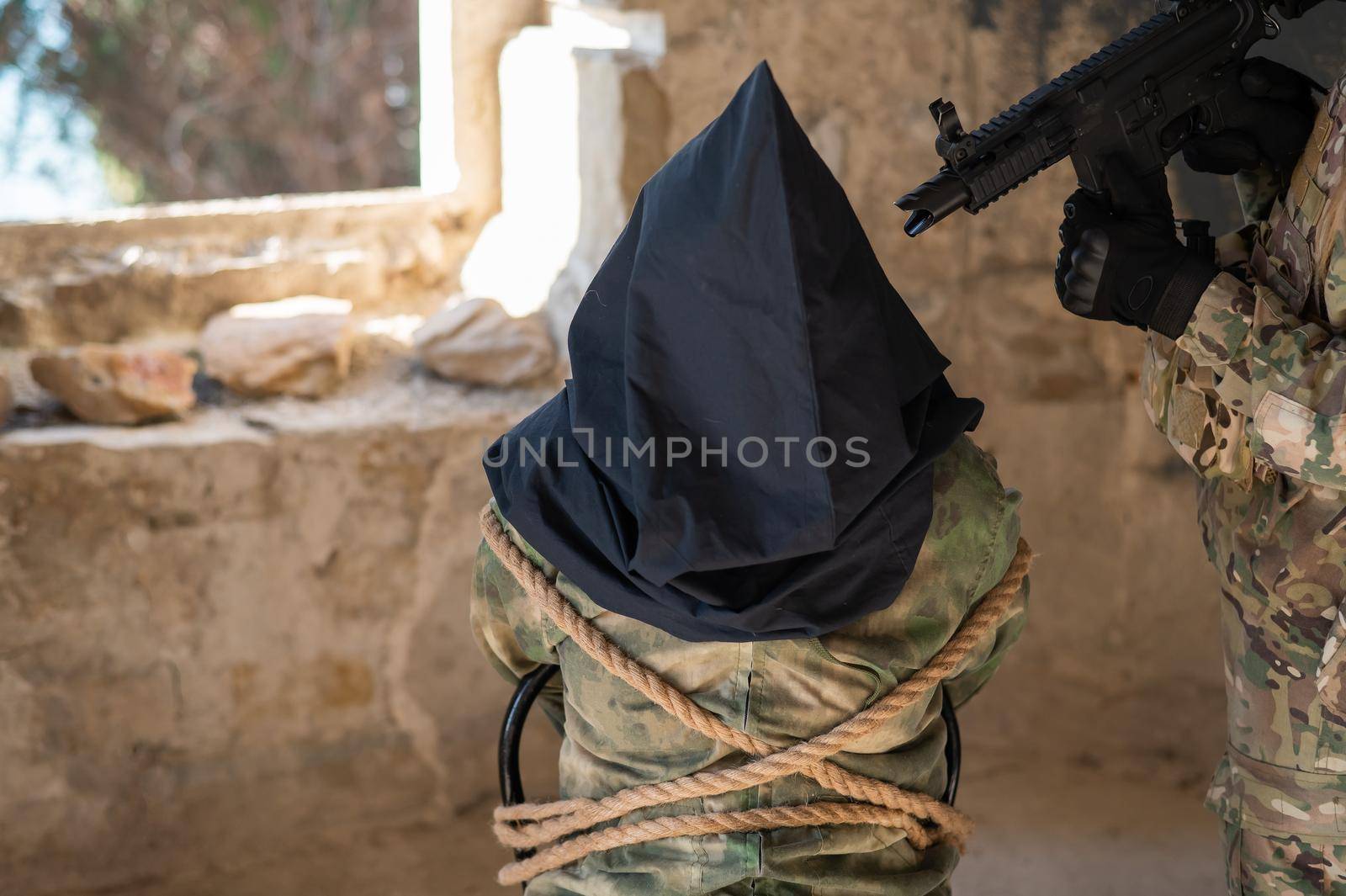 A caucasian woman in an army uniform holds a hostage with a bag on her head at the sight of a machine gun. by mrwed54