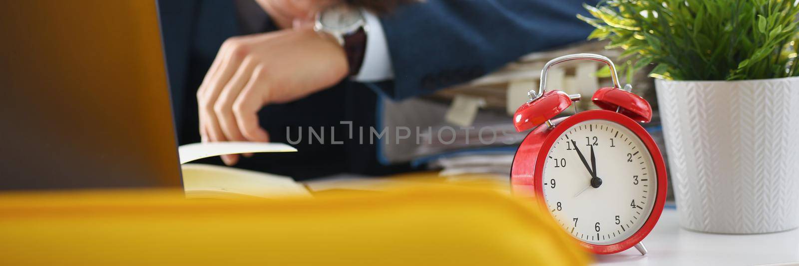 A man sleeps in the workplace, an alarm clock in the foreground. Work fatigue, deadline. Emotional burnout, stress