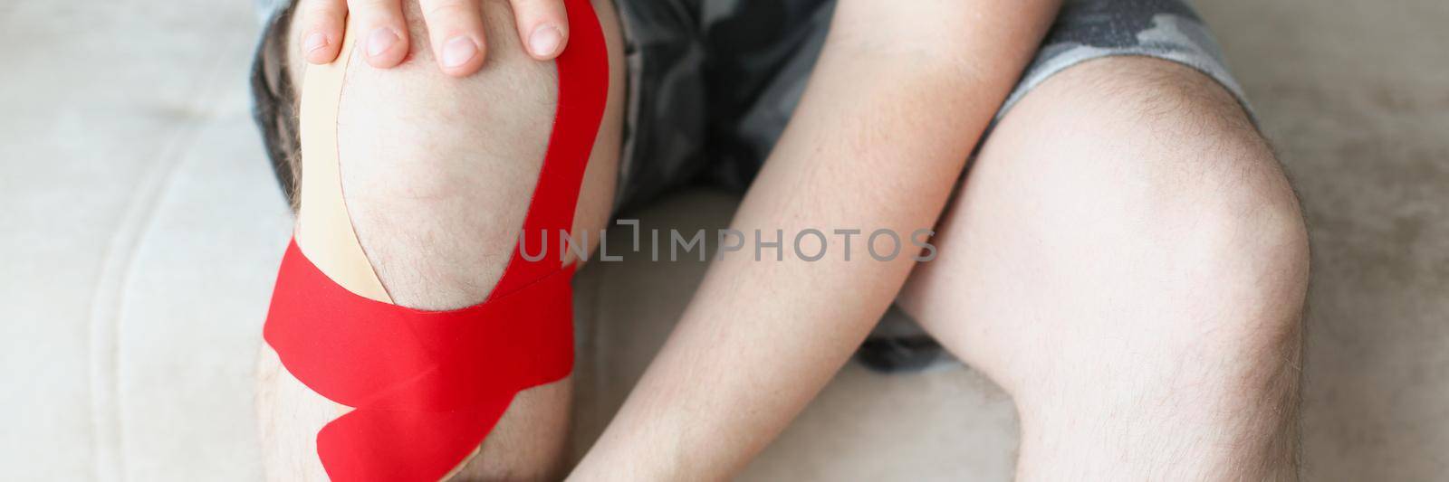 A man sits with a kinesiology tape on his knee, legs close up. Supports knee muscles. Ligament sprain, postoperative rehabilitation