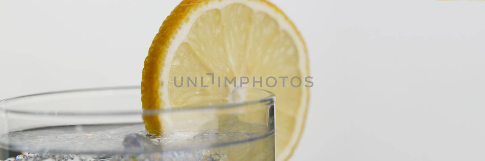 A glass of soda water with a slice of lemon, close-up. Toning drink with ice on gray background, slimming product
