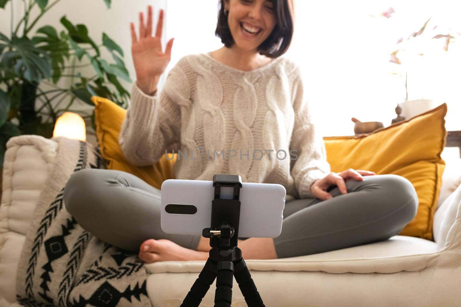 Smiling young caucasian female influencer live streaming at home waving hello to social media followers. Social media concept.