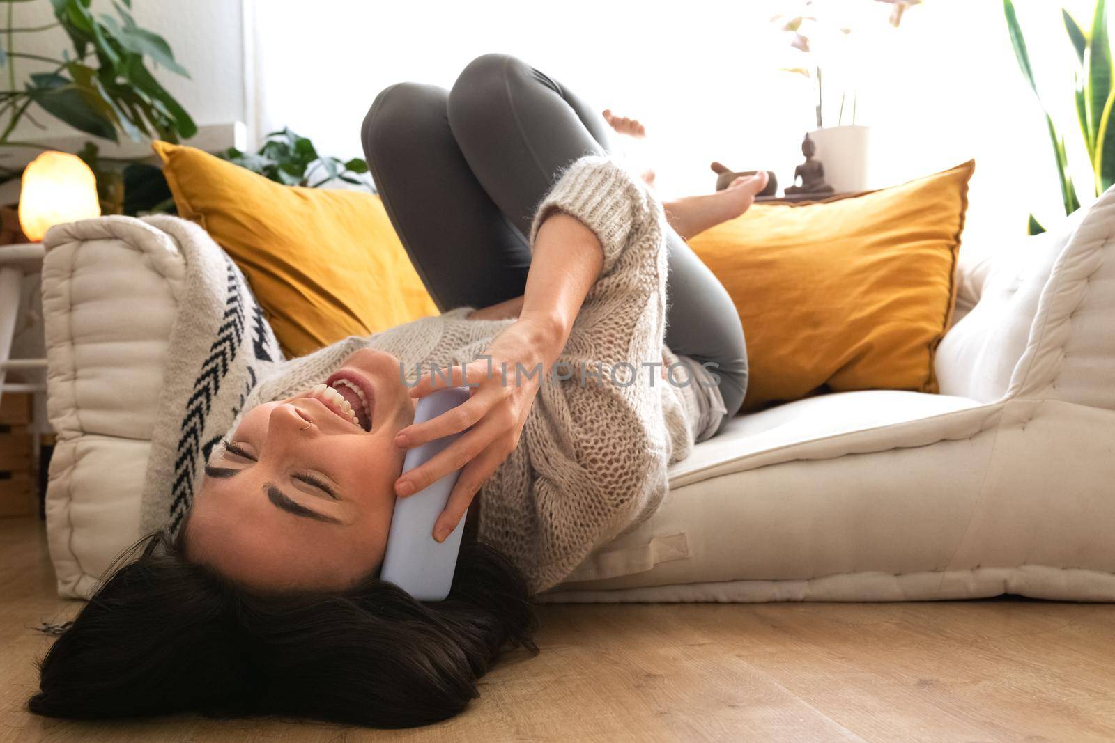 Happy young caucasian woman lying upside down on the couch talking on cellphone laughing. Copy space. Happiness concept.