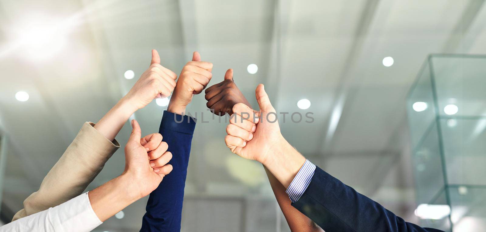 Thumbs up to success. Shot of a group of hands showing thumbs up in an office. by YuriArcurs
